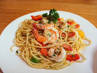 Spaghetti pasta with shrimp and sweet basil in white plate on wooden table texture