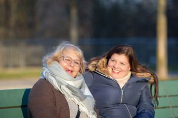 Fototapeta premium Business women talk to each other while sitting on a Bech of a city park. They are posing for the camera.