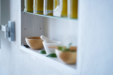 still life, bright and sunny detail of shelf in kitchen blurred in house with bottles olive oil wooden bowl mortar green mediterranean style mood