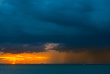 Ships in the sea on a background of clouds with rain during sunset / sunrise. The sun on the horizon. Rain at sea during sunset / sunrise. Contrast blue and yellow