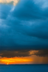 Ships in the sea on a background of clouds with rain during sunset / sunrise. The sun on the horizon. Rain at sea during sunset / sunrise. Contrast blue and yellow