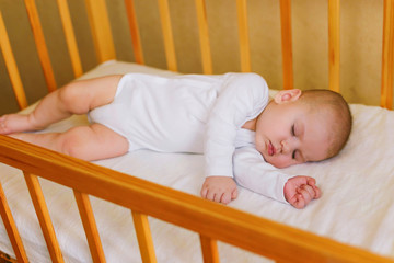 Portrait of a beautiful little boy 5 months old in white clothes, sleeping in his crib. Childhood dreams. Concept of health and children. Selective focus.
