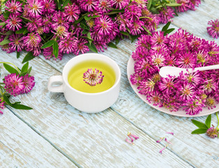 Traditional Herbal Tea of Red Clover Flowers (Trifolium pratense). Fresh Clover Flower Tea in a white cup. Purple Wildflowers bouquet on a wooden rustic table. Phytotherapy Medicinal Herbs