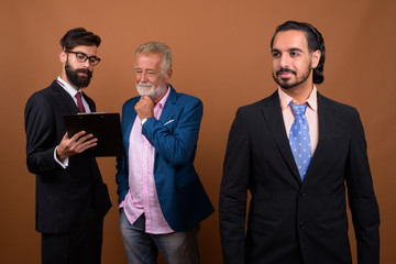 Three multi ethnic bearded businessmen together against brown background