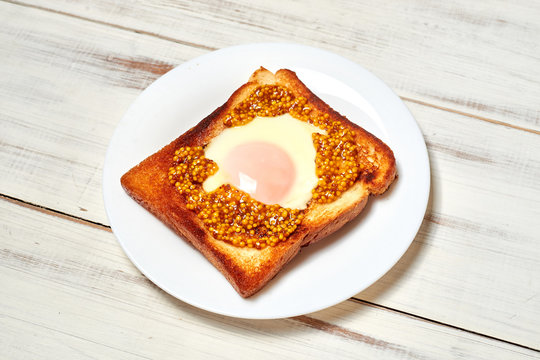 Toast with an egg on a plate on a light wooden background.