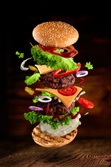Maxi hamburger, double cheeseburger with flying ingredients isolated on wooden background. High resolution image