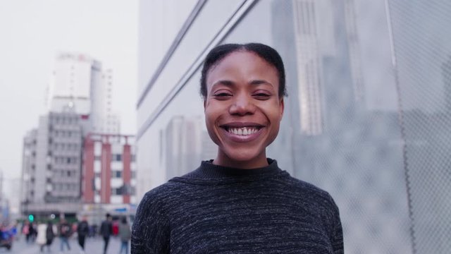 Close up of pretty young African woman portrait one beautiful Black lady looking at camera smile in the urban China city street with Chinese people walking in the background