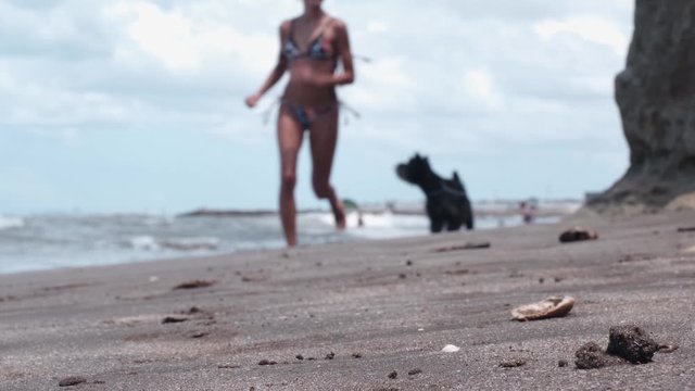 a young girl running next to her little black dog on the beach