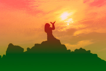 Silhouette of woman praying over beautiful sky background.