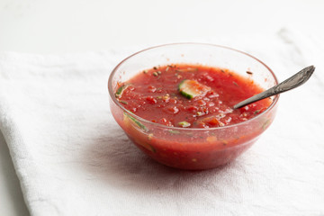 Bowl with spoon of fresh gazpach soup with tomatos, cucumber, spices on white backgrouns