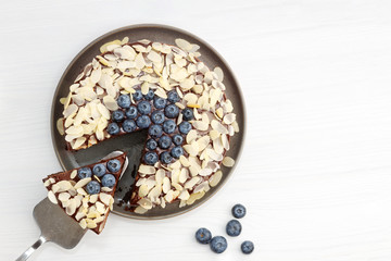 Homemade chocolate cheesecake with blueberries and almond slices on white wooden table. Top view. Copy space.