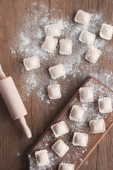 Uncooked ravioli with meat on a brown wooden board. The process of cooking homemade ravioli.