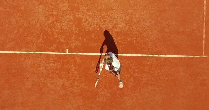 Tennis player hitting the ball on the red court. Summer sport concept. Top aerial view footage. 