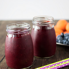 Fruit and berry smoothies and fresh apricots, raspberries and blueberries on an oval metal plate. Gray background.