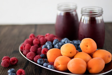 Fruit and berry smoothies and fresh apricots, raspberries and blueberries on an oval metal plate. Gray background.