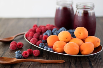 Fruit and berry smoothies and fresh apricots, raspberries and blueberries on an oval metal plate. Gray background.