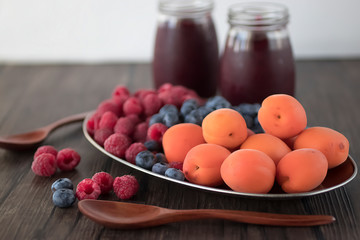 Fruit and berry smoothies and fresh apricots, raspberries and blueberries on an oval metal plate. Gray background.