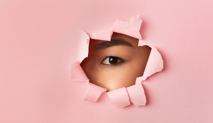 Asian female eye without mascara looking through torn paper