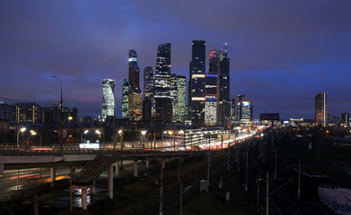 Fototapeta na wymiar City landscape with many railroad tracks going far, cars on the overpass and skyscrapers with towers of Moscow CIty with lighting windows in the evening