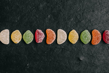 Naklejka premium Close up view of fruity sugary candies on black slate background with selective focus. 
