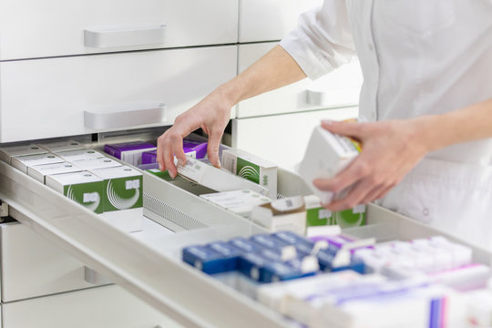 Pharmacist holding medicine box and capsule pack in pharmacy drugstore.
