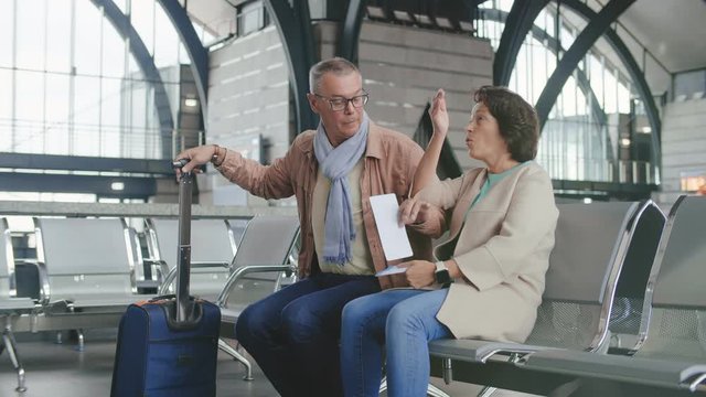 Portrait of cheerful elderly couple sitting in waiting area and waiting for their flight boarding