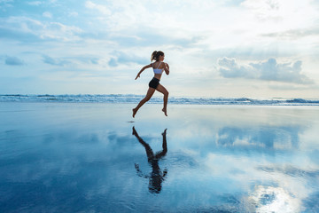 Barefoot young girl with slim body running along sea surf by water pool to keep fit and burning...