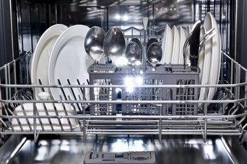 The lower shelf of the dishwasher basket is pushed forward in an orderly filled with pure sparkling utensils.