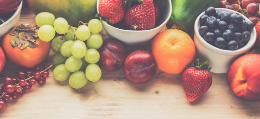 Healthy colorful fruits berries, strawberries oranges plums grapes mango papaya red currants peaches on wooden table, top view, toned, banner, selective focus