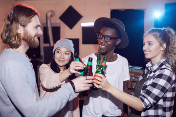 Multi-ethnic group of young people drinking beer and chatting while enjoying rehearsal in music studio, shot with flash