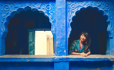 Asian woman looking out blue window frame during her vacation in Jodpor, Jodhpor is one of the most...