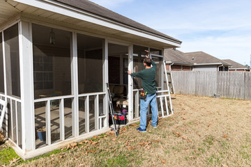 Fototapeta na wymiar Repairman uses hammer to repair door on screened in back porch