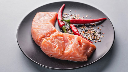 Food banner. Fresh salmon slice, herbs, spices and hot peppers on a dark plate.