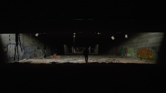 Silhouette Of Adult Male Walking Into Light Of Large Abandoned Warehouse. Slow Motion