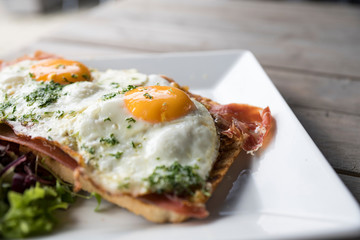 Meat sandwicht with fried eggs, salad on white plate and wooden table