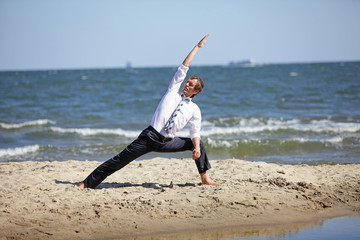 Obraz premium Caucasian business man practicing yoga on the beach