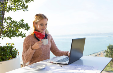 business woman working on laptop while drinking coffee outside