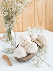 bolas de helado sobre cuenco de coco en mesa blanca y con flores