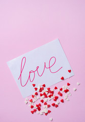 pastry sprinkles in the form of hearts  scattered on a post card love on pink background. Valentine's day.