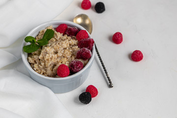 Breakfast consisting of oatmeal, nuts and fruits. Kiwi raspberries blackberries pomegranates almonds mint decorate a plate. Healthy eating, on a light background.