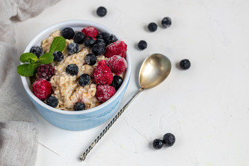 Breakfast consisting of oatmeal, nuts and fruits. Kiwi raspberries blackberries pomegranates almonds mint decorate a plate. Healthy eating, on a light background.