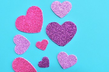Creative card for Valentine’s Day with shiny paper colorful hearts on turquoise background. Sparkle purple, pink and violet heart on blue paper backdrop. Romantic background. Dating concept 