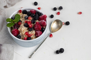 Breakfast consisting of oatmeal, nuts and fruits. Kiwi raspberries blackberries pomegranates almonds mint decorate a plate. Healthy eating, on a light background.
