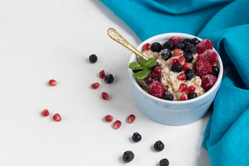 Breakfast consisting of oatmeal, nuts and fruits. Kiwi raspberries blackberries pomegranates almonds mint decorate a plate. Healthy eating, on a light background.