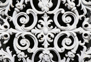 Vintage wrought iron grate with ornate floral pattern, painted white, against a black background.