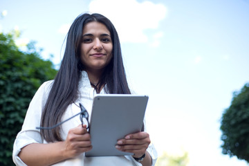 Fototapeta premium portrait of an indian girl. Business lady holding glasses and tablet in her hands. Outdoors