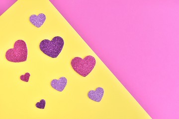 Greeting card for Valentine’s Day with pink and purple shiny paper hearts on yellow and pink background. Sparkle hearts on color blocks backdrop with empty space for text. Romantic background. 