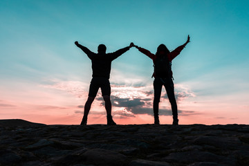 Couple silhouette with raised arms holding hands and looking at sunset