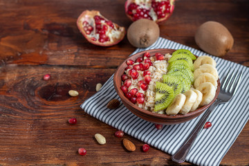 Breakfast consisting of oatmeal, nuts and fruits. Kiwi banana pomegranate almonds decorate a plate. Healthy food, on wooden background.