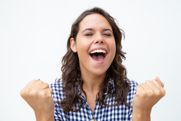 Excited young woman raising fists. Beautiful cheerful young woman with closed eyes celebrating success. Winner concept